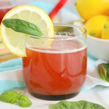 Rhubarb cordial served in a glass with lemon slice garnish and fresh basil.