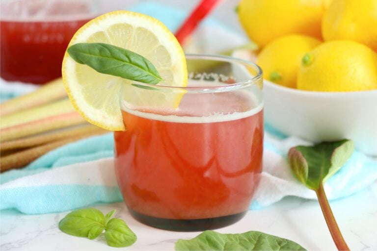 Rhubarb cordial served in a glass with lemon slice garnish and fresh basil.