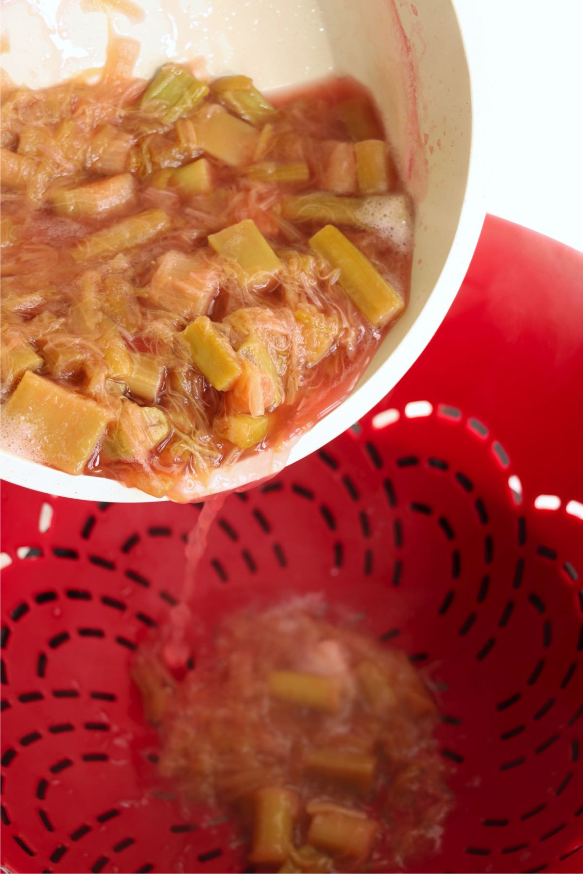 Cooked rhubarb mixture being strained through a colander.