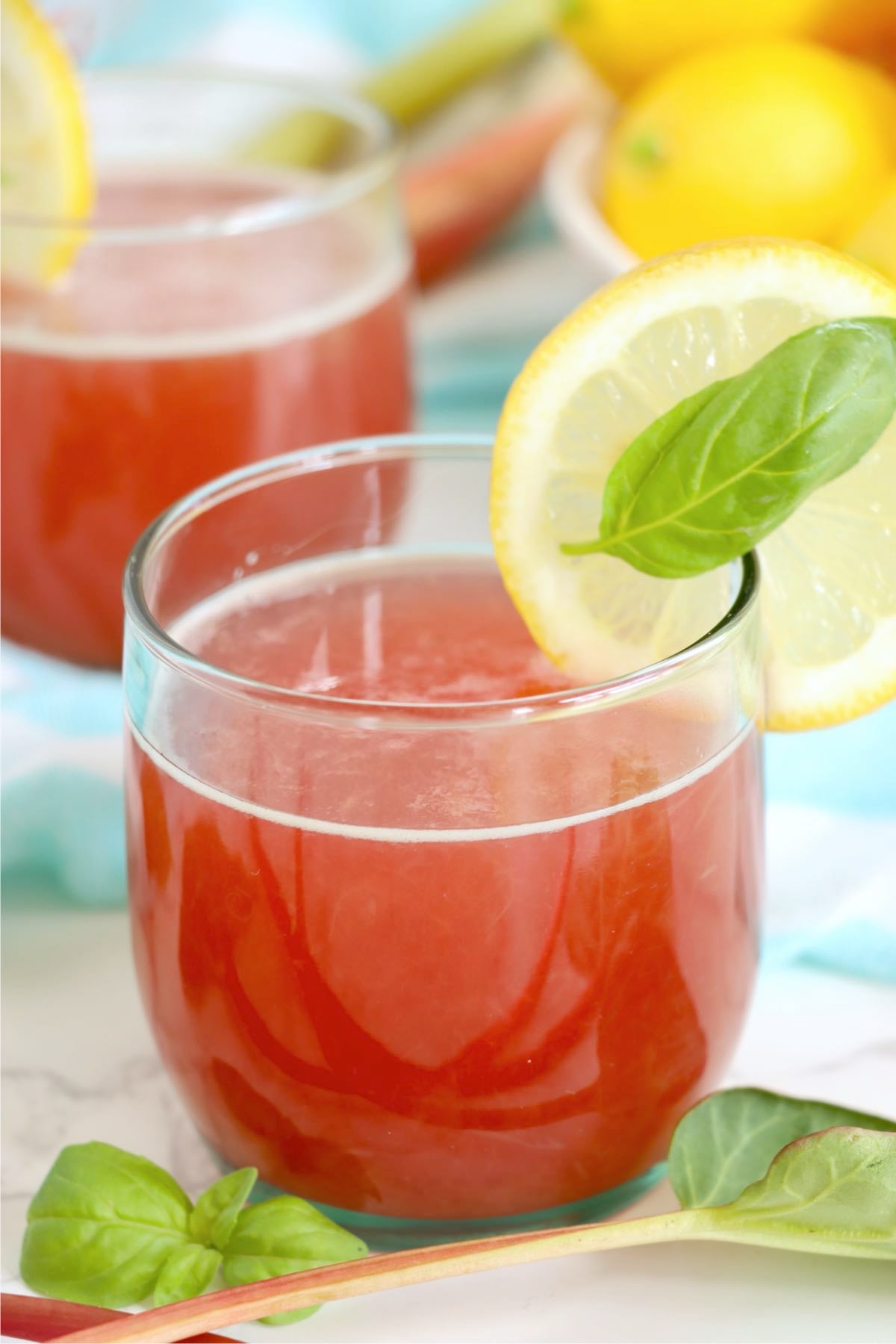 Homemade rhubarb cordial served in a clear glass with lemon garnish.