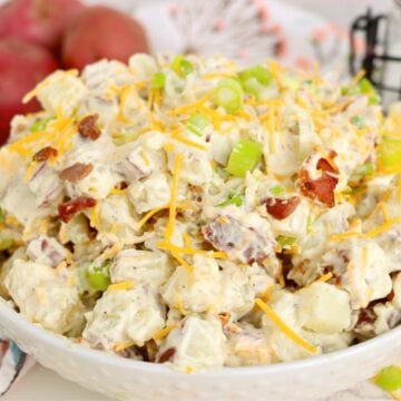 Serving bowl filled with creamy potato salad garnished with cheddar cheese, bacon and sliced green onions.