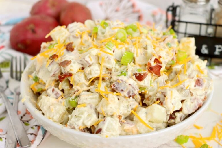 Serving bowl filled with creamy potato salad garnished with cheddar cheese, bacon and sliced green onions.
