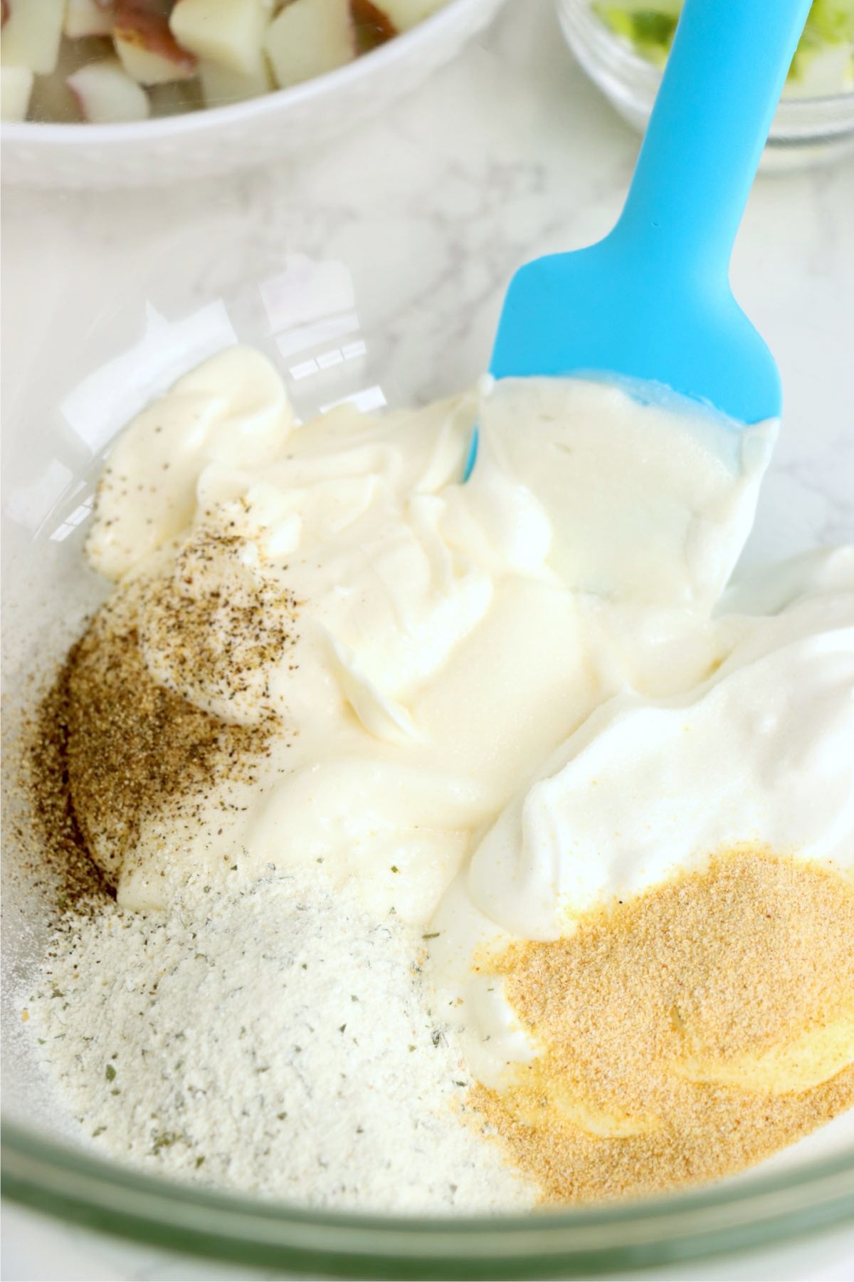 Mayonnaise, sour cream, ranch seasoning, garlic powder, salt and black pepper added to a glass mixing bowl before stirring.