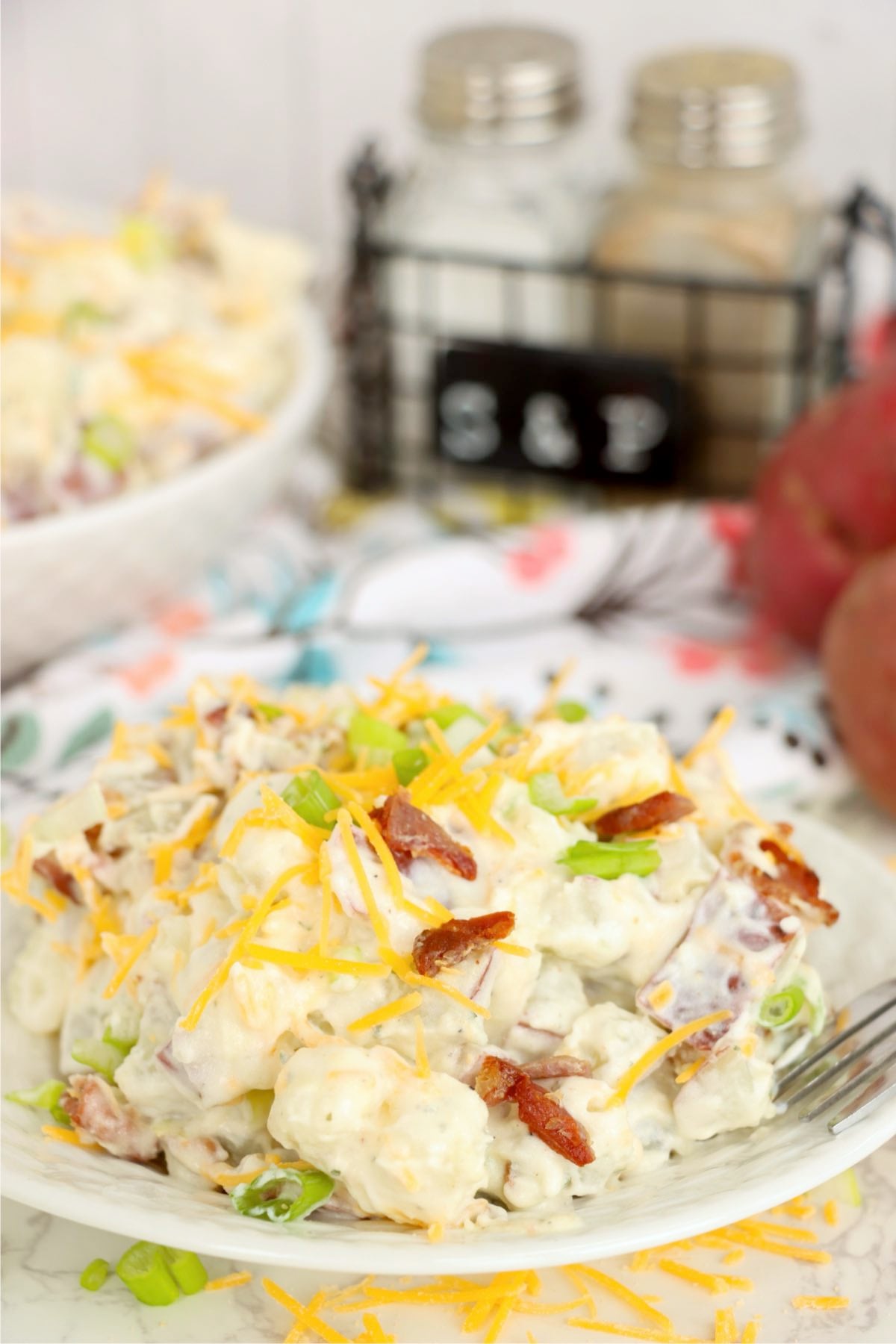 Creamy potato salad topped with shredded cheddar cheese, bacon pieces and fresh green onions.