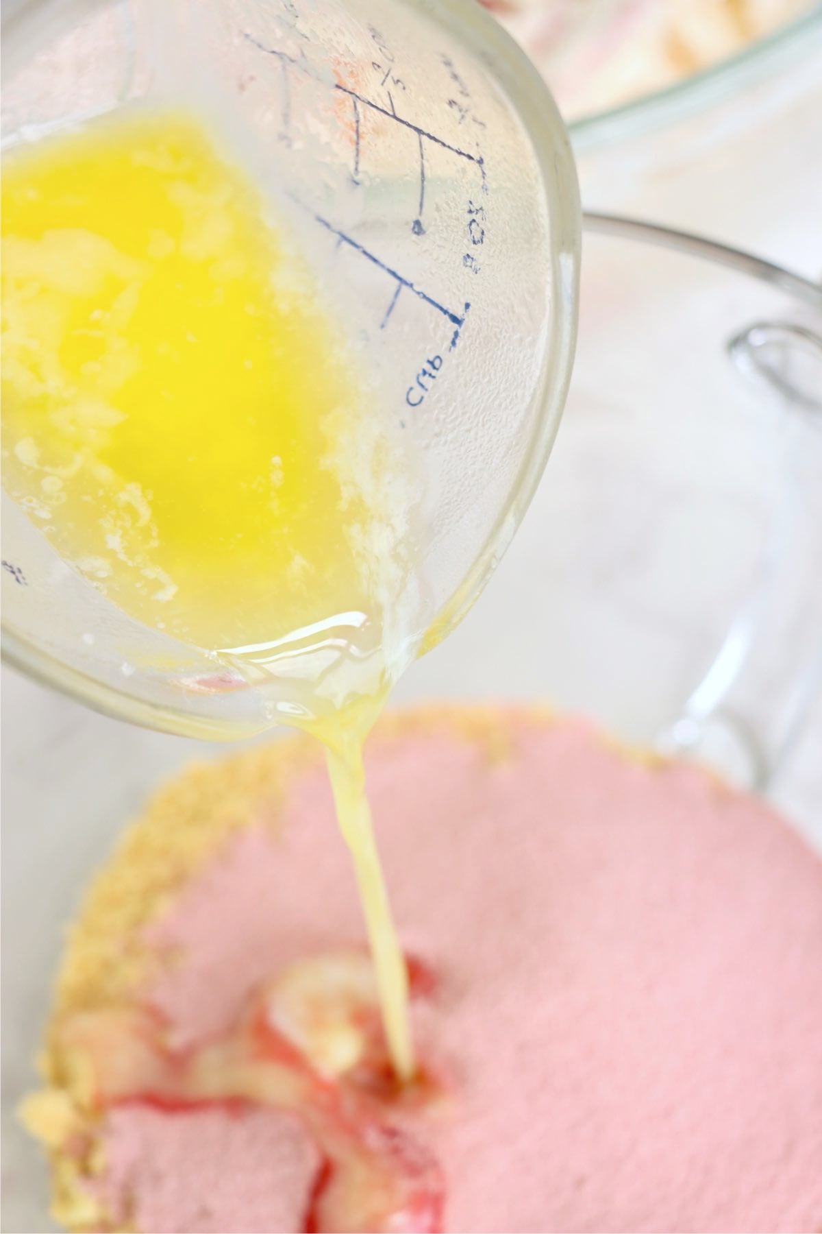 Melted butter being poured into strawberry cheesecake mixture.