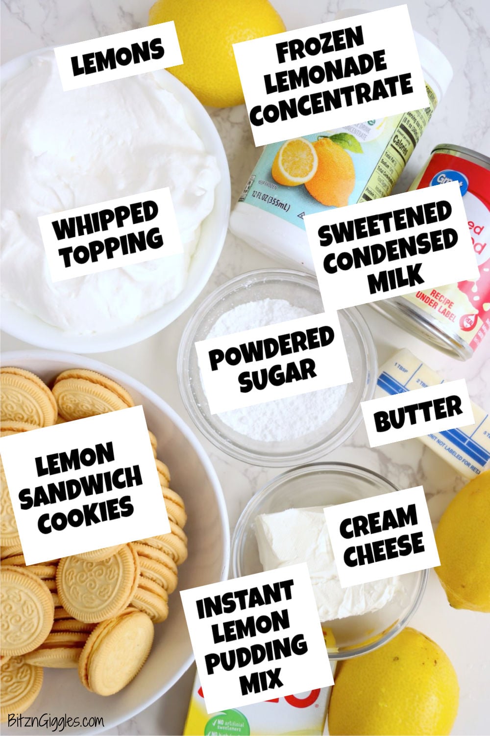 Lemons, lemon sandwich cookies, whipped topping, cream cheese, butter, powdered sugar, pudding mix, condensed milk and lemonade concentrate arranged on a pale marble surface.