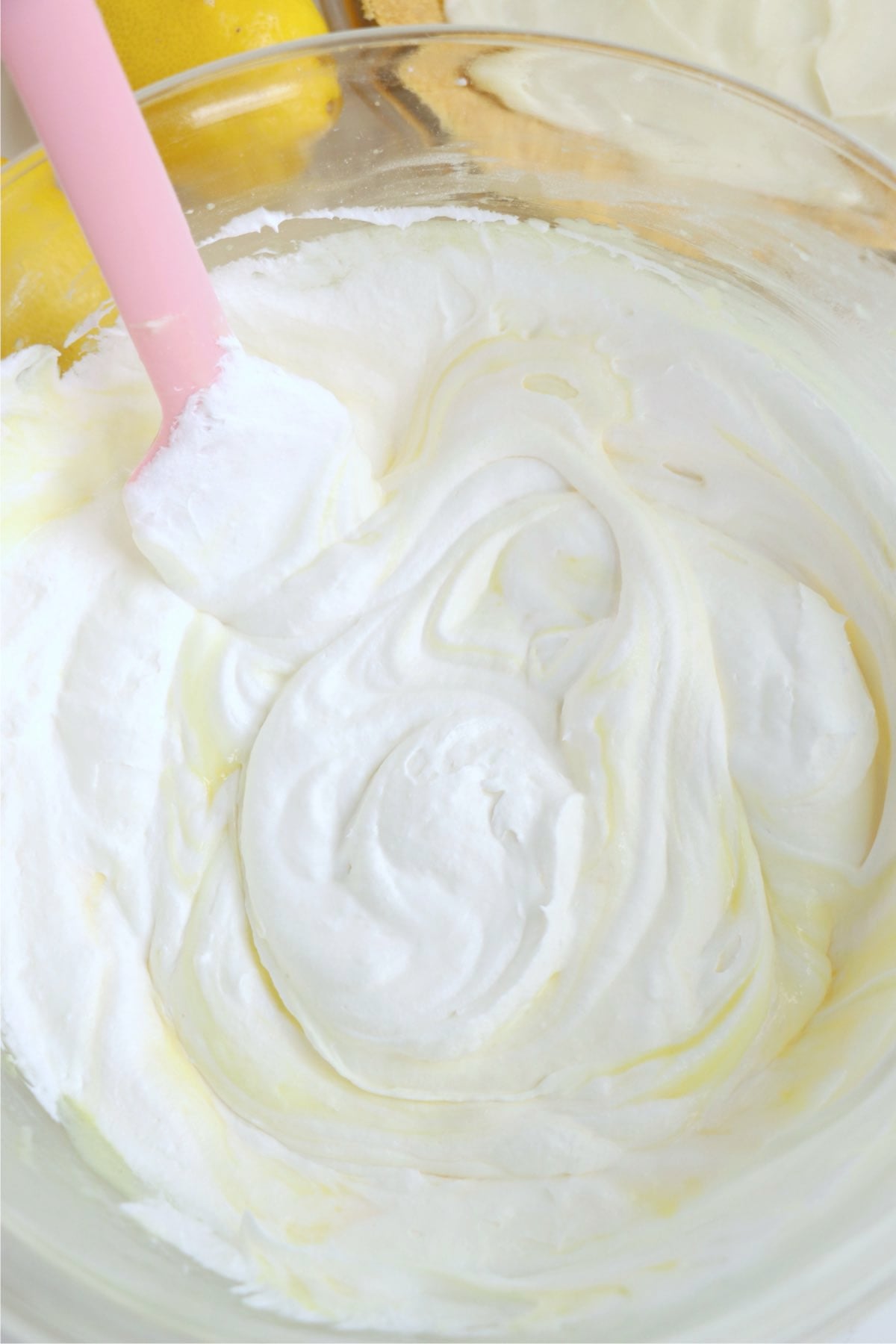 Pink spatula stirring whipped topping in a glass bowl.