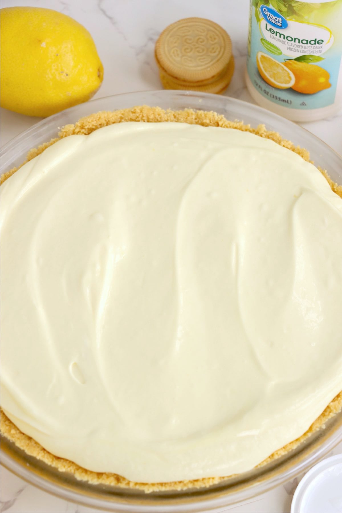 Lemon filling spread evenly inside golden cookie crust in clear pie plate.