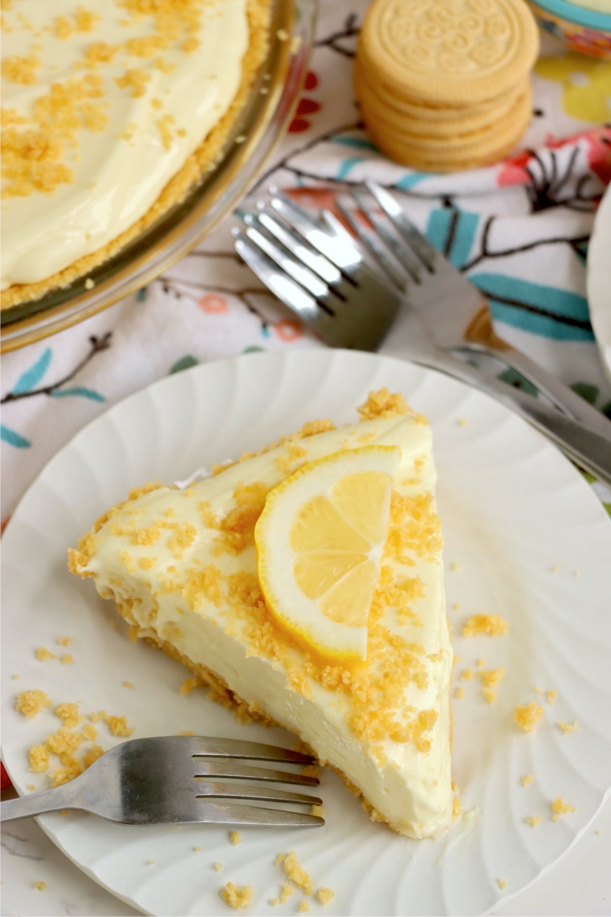 Creamy pie slice topped with lemon wedge and golden crumbs on white plate beside fork.