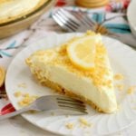 Frozen lemonade pie slice with lemon wedge, cookie crumbs and buttery crust.
