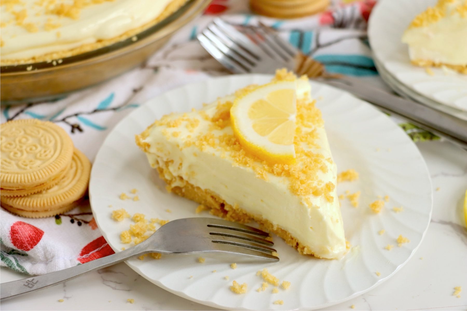 Frozen lemonade pie slice with lemon wedge, cookie crumbs and buttery crust.
