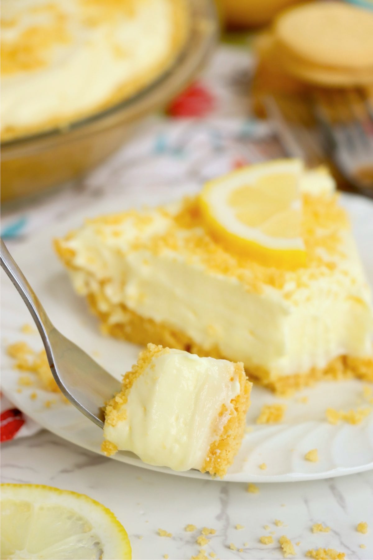 Plated lemonade pie slice surrounded by golden sandwich cookies, crumbs, forks and remaining pie.