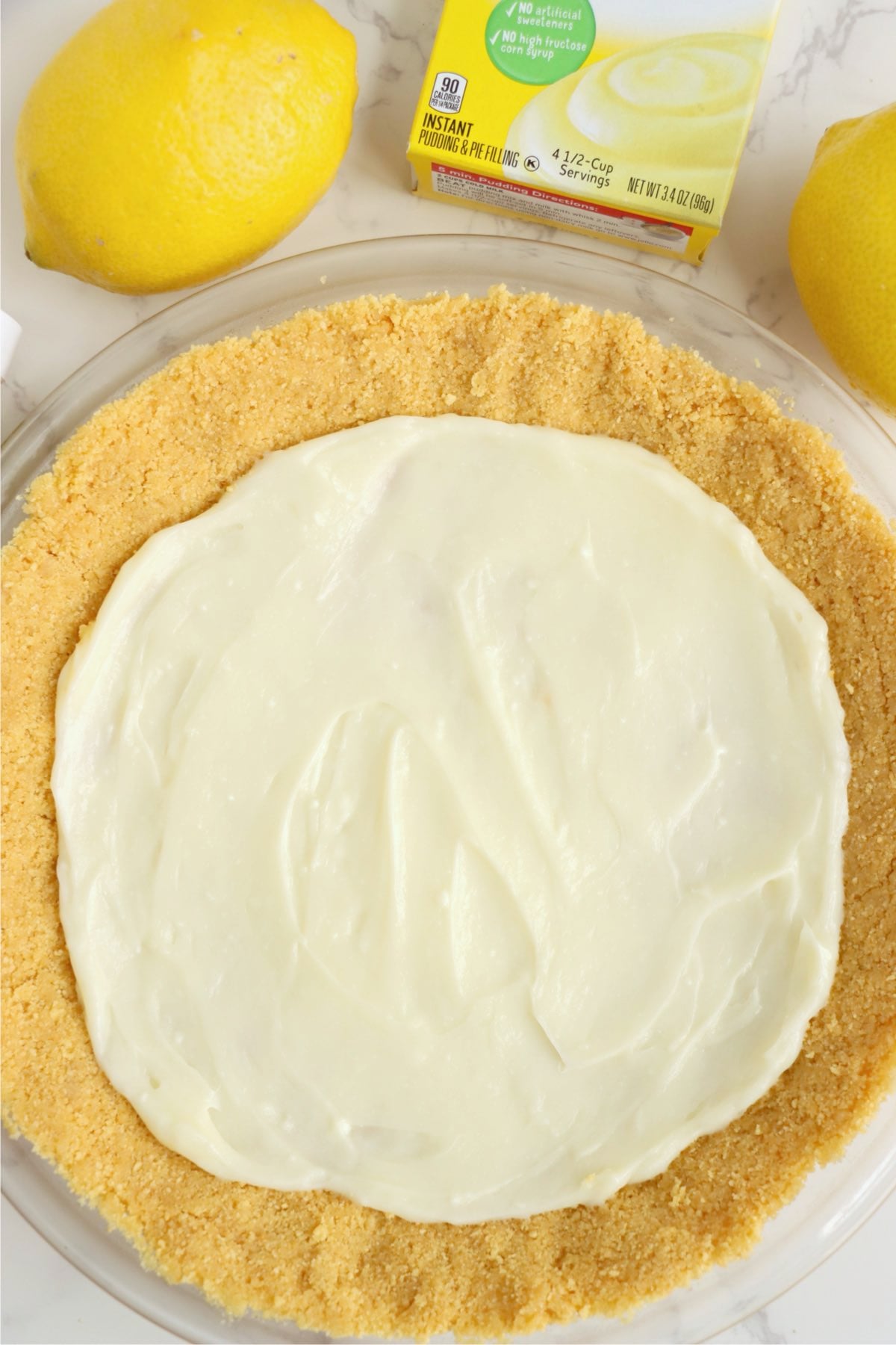 Smooth white cream cheese layer spread across pressed golden cookie crust in glass pie plate.