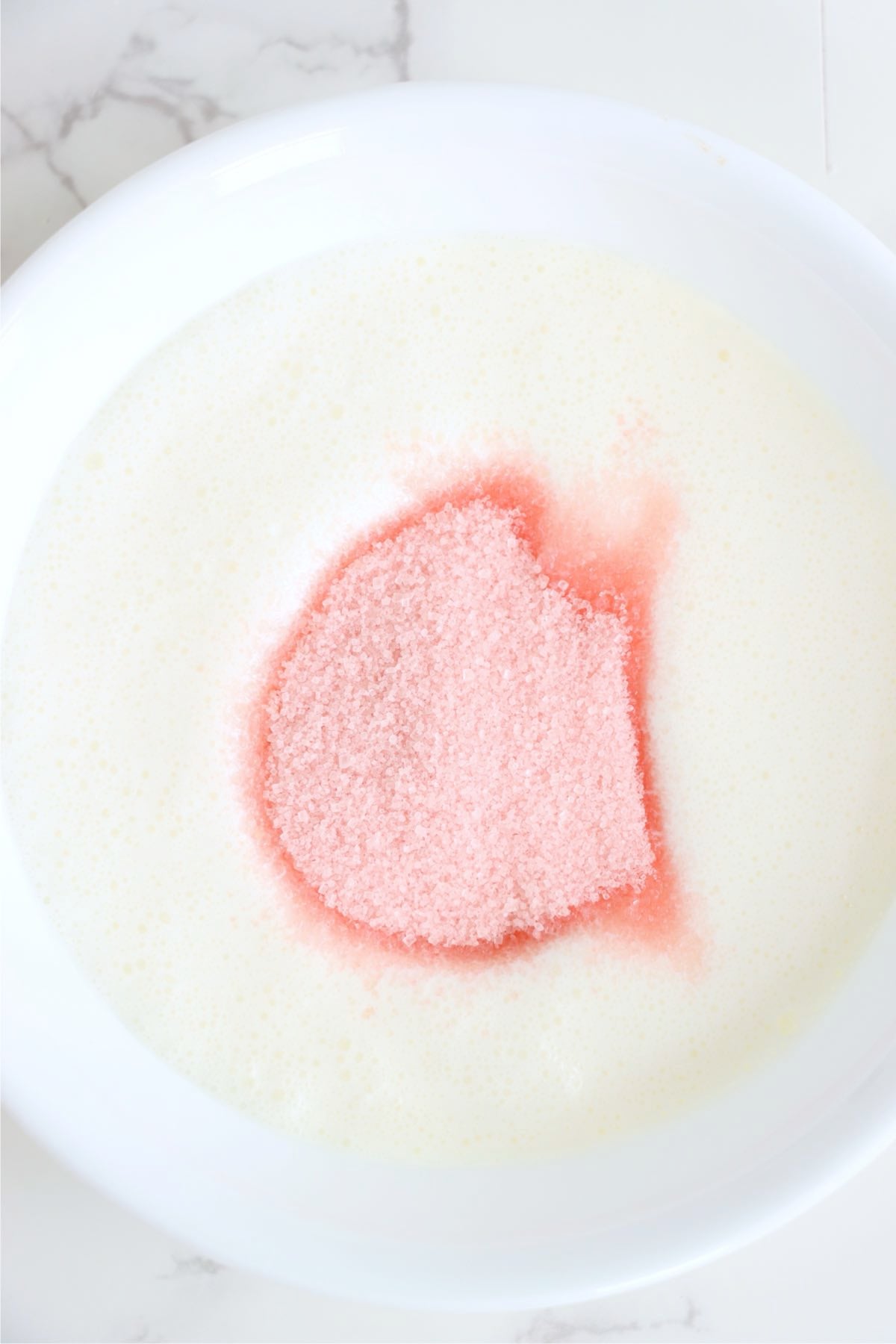 Heavy whipping cream topped with pink lemonade mix in a white mixing bowl.