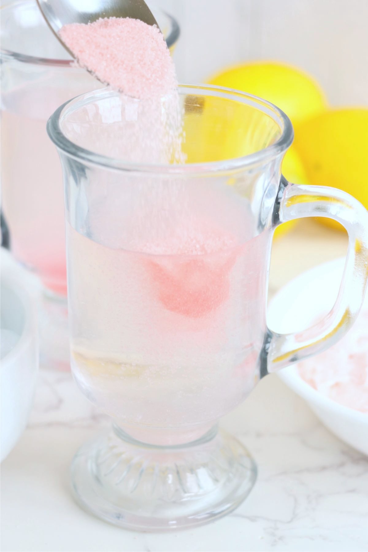 Pink lemonade mix being poured into a glass mug filled with water.
