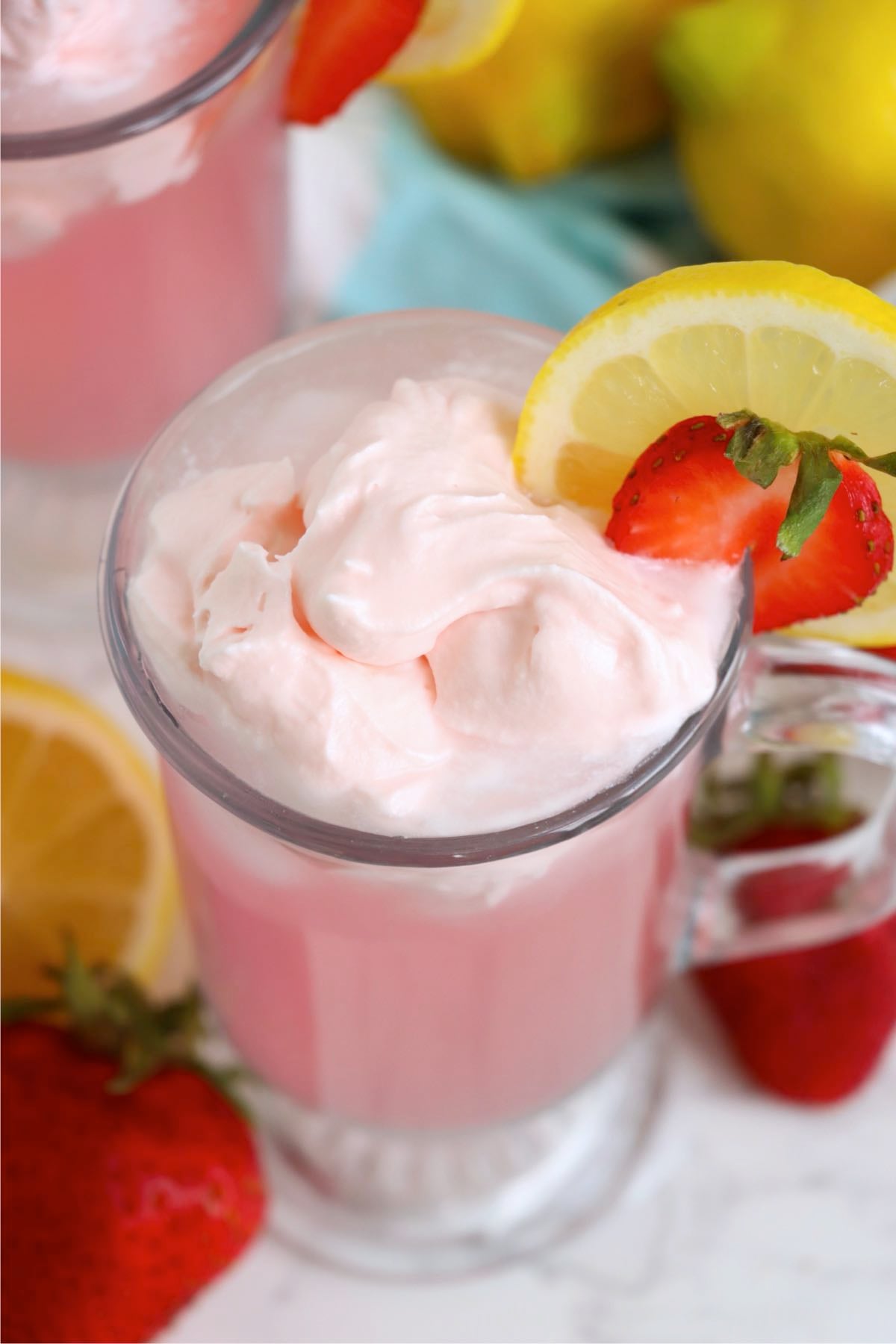 Whipped cream topping with strawberry and lemon slice on pink lemonade.