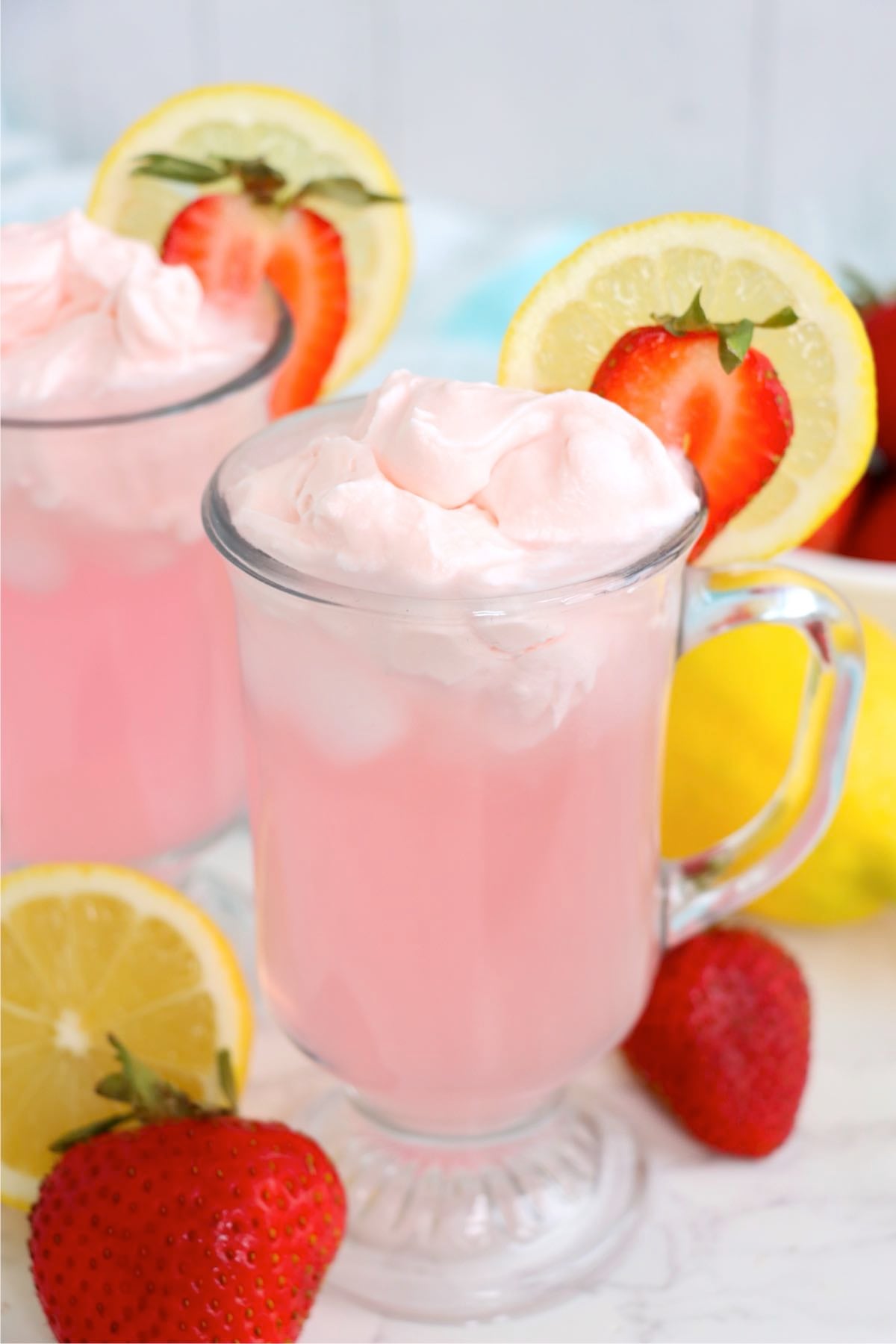 Pink lemonade topped with whipped cream, lemon slice and fresh strawberry garnish.