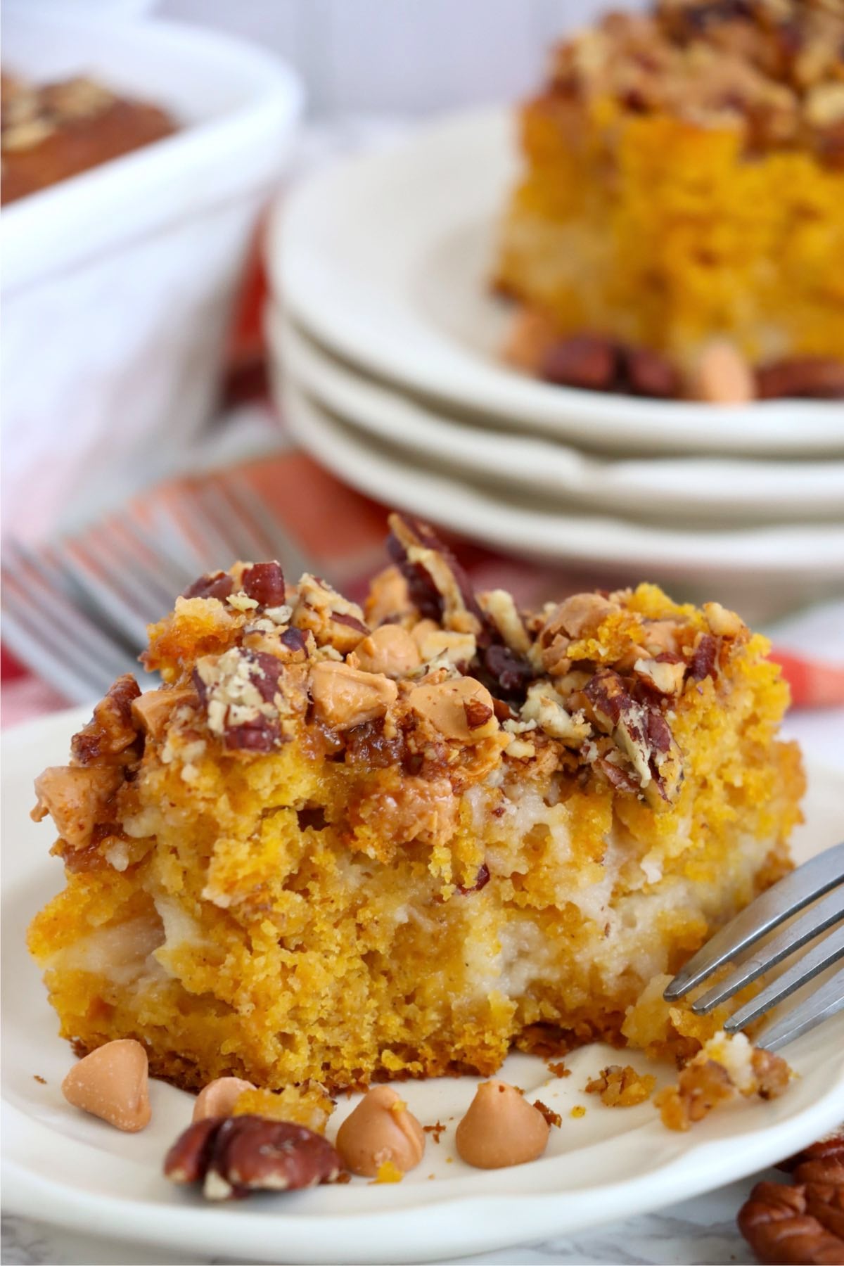 Fork rests beside a partly eaten pumpkin cake slice with cream cheese pockets, pecans and butterscotch chips.