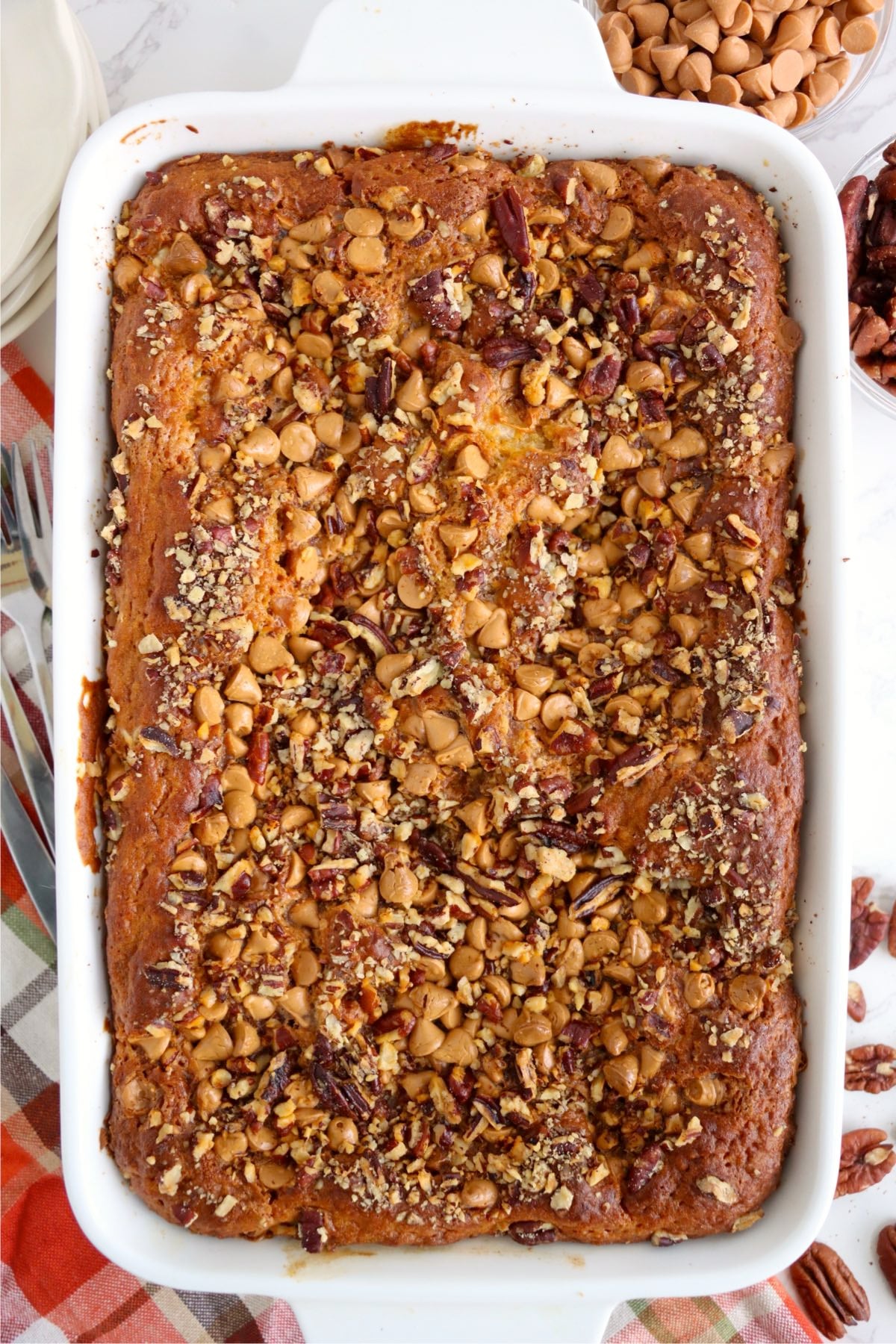 Baked golden-orange cake sits in a white casserole dish with toasted pecans and melted butterscotch chips.