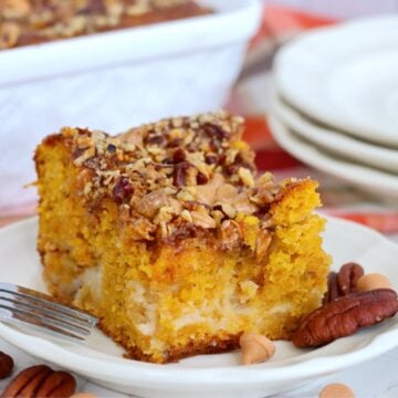 Square of pumpkin earthquake cake with cream cheese ribbons, chopped pecans and butterscotch chips sits on a white plate.