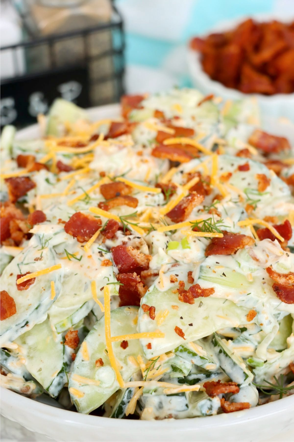 Creamy cucumber slices topped with shredded cheddar, crisp bacon, green onions and fresh dill in a white bowl.