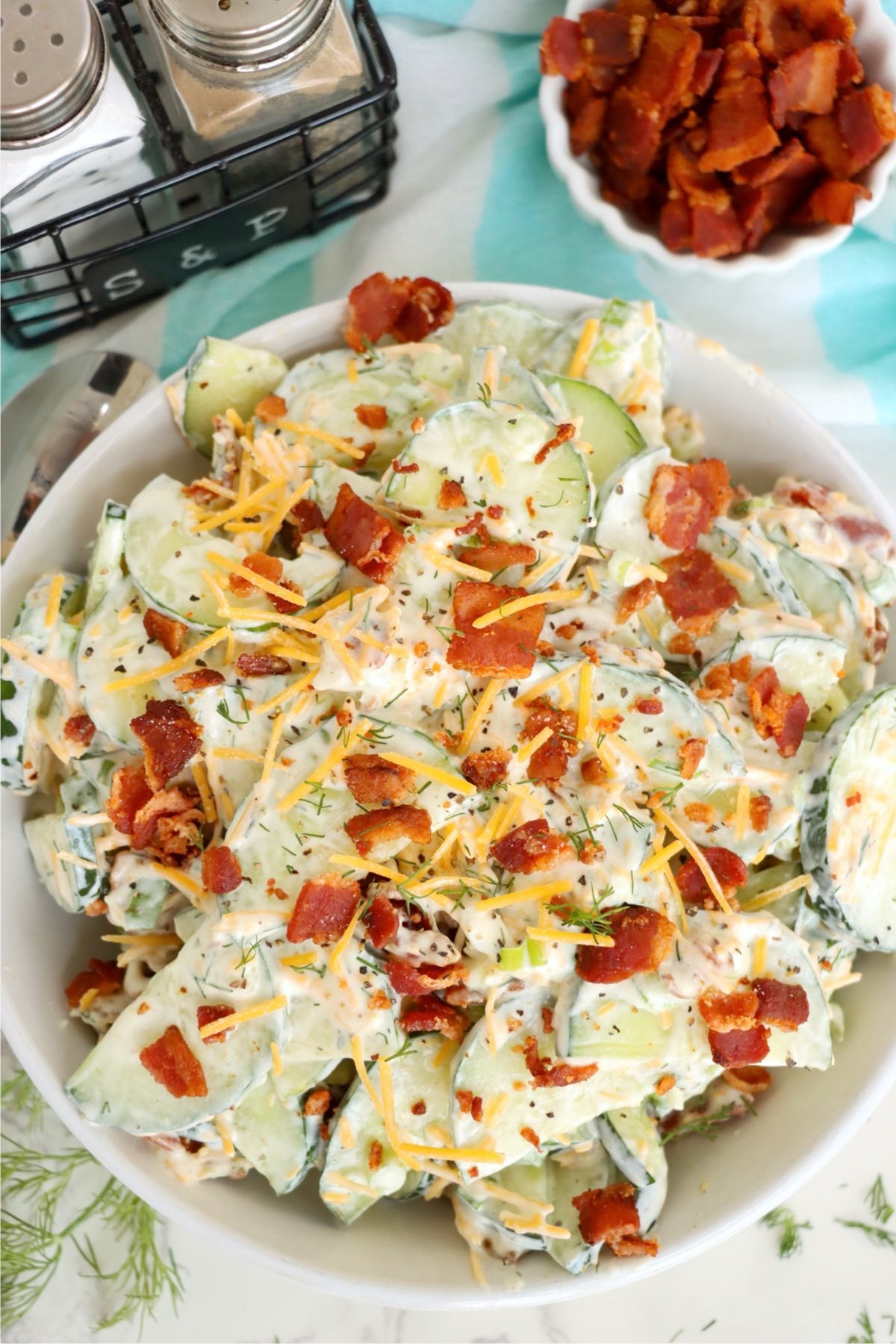Creamy cucumber salad topped with crumbled bacon, shredded cheddar and fresh dill.