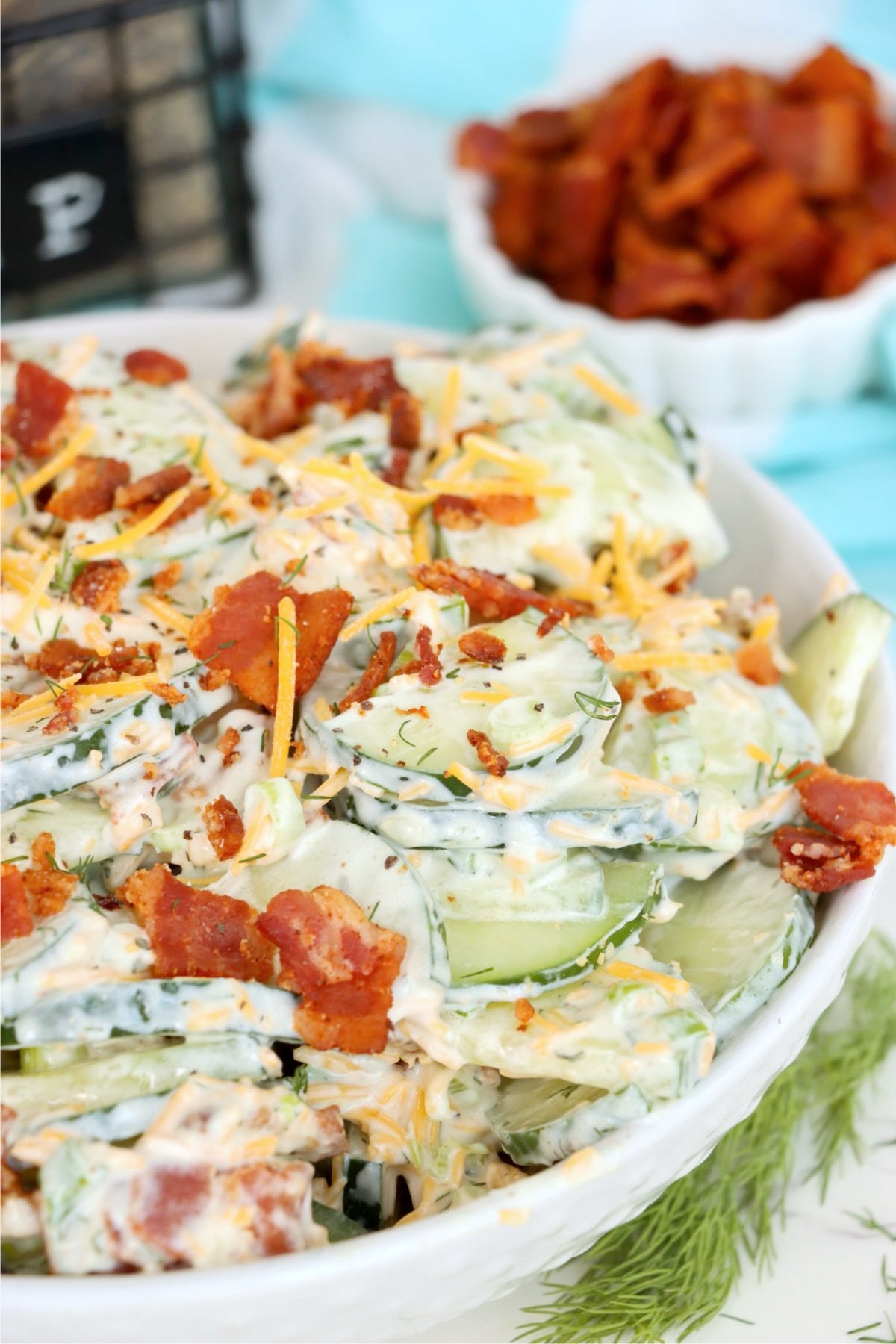 Creamy cucumber half-moons layered with crisp bacon, shredded cheddar and fresh dill in a white bowl.