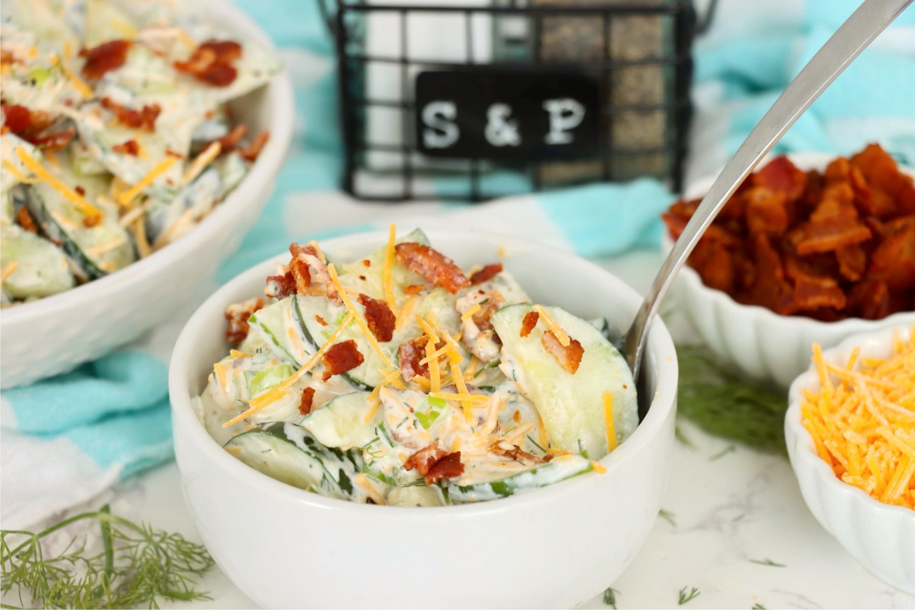Creamy cucumber half-moons layered with crisp bacon, shredded cheddar and fresh dill in a white bowl.
