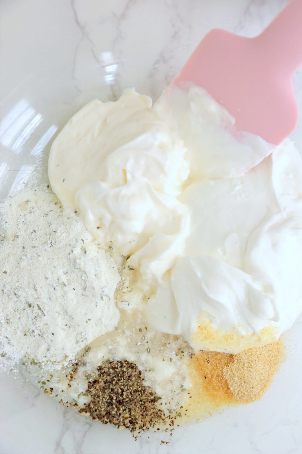 Sour cream, mayonnaise, ranch seasoning, garlic powder and black pepper arranged in a large mixing bowl.
