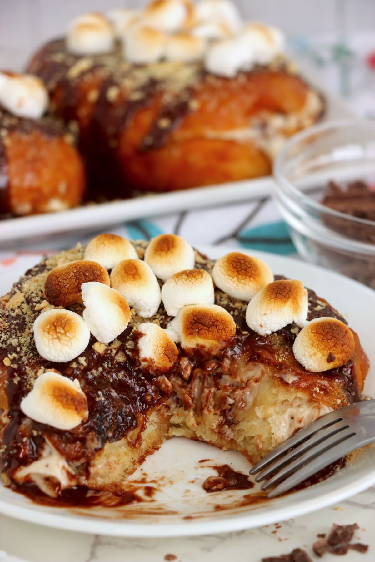 Partially eaten stuffed croissant showing creamy chocolate filling beneath toasted marshmallows, graham crumbs and chocolate sauce.
