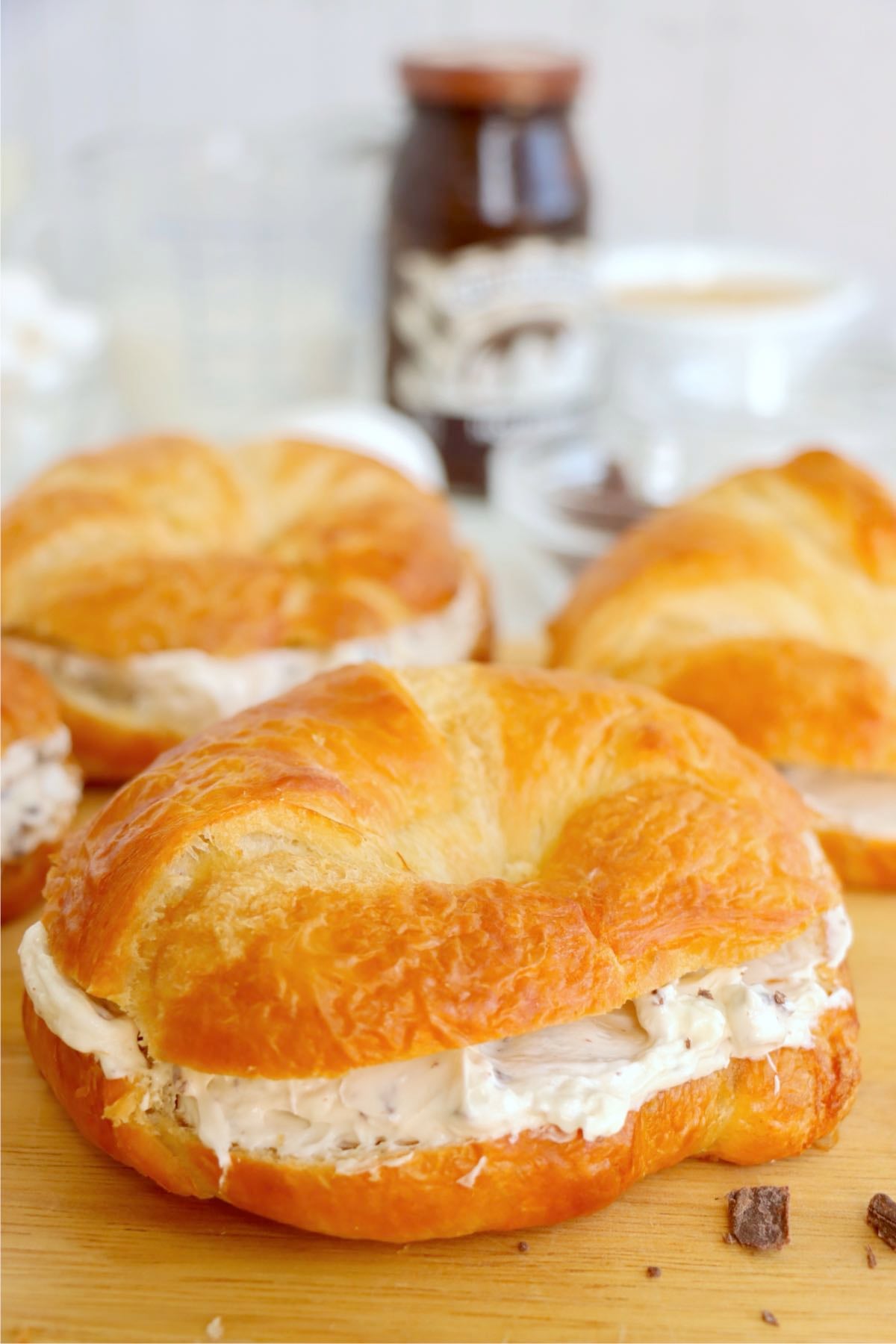 Golden croissants split and filled with thick white chocolate-speckled cream on a wooden cutting board.