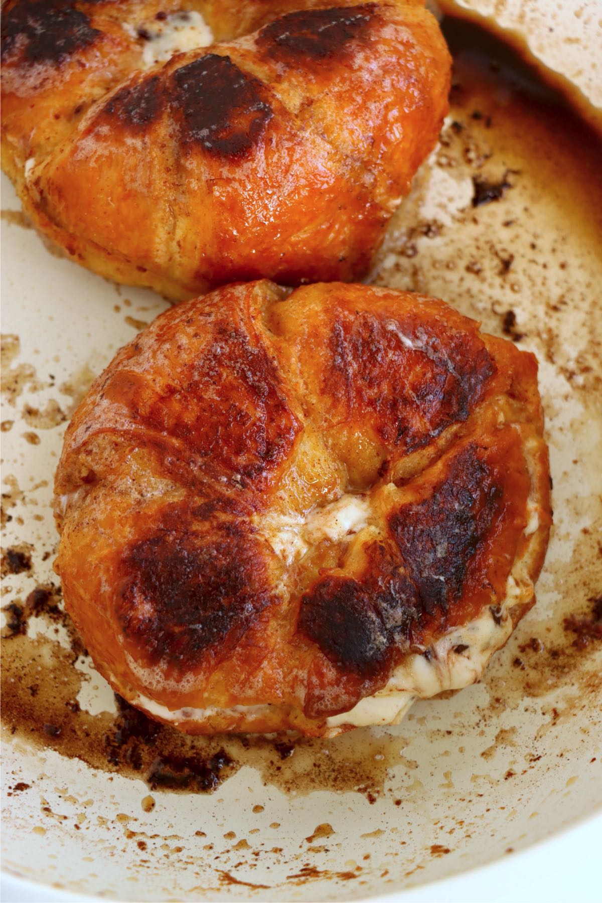 Stuffed croissants browning in a skillet with caramelized tops and creamy filling peeking from the sides.