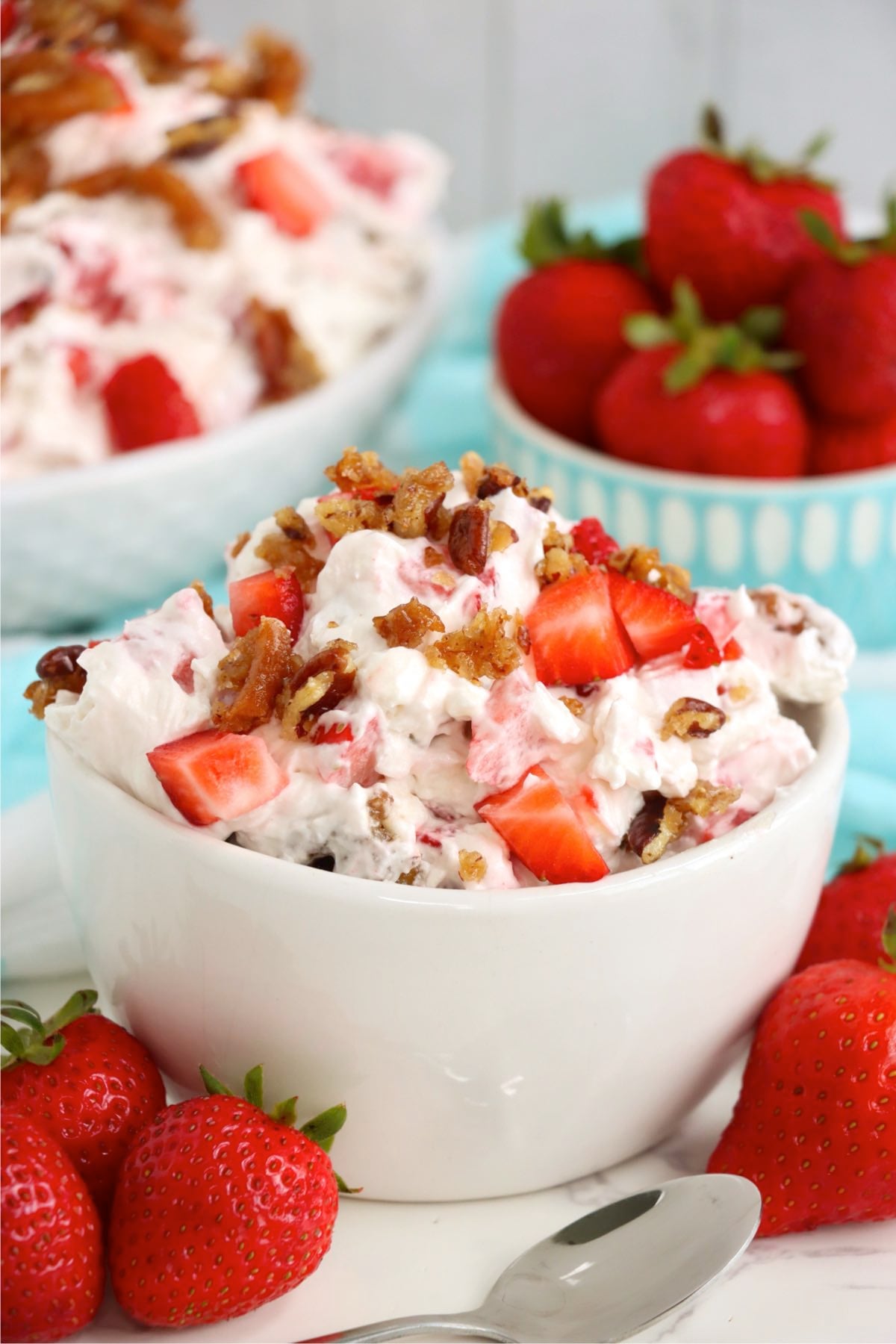Individual bowl of creamy strawberry dessert topped with diced strawberries and caramelized pretzel-pecan pieces.