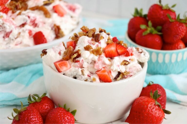 Individual bowl of creamy strawberry dessert topped with diced strawberries and caramelized pretzel-pecan pieces.