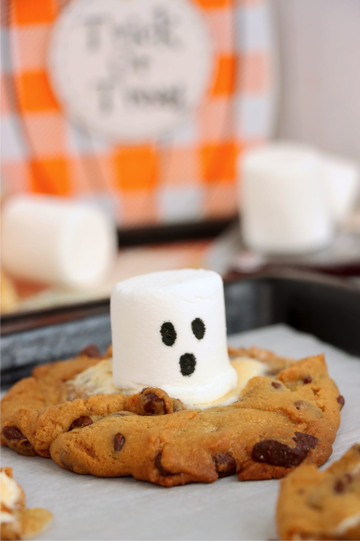 Marshmallow ghost sitting in the center of a golden brown chocolate chip cookie.