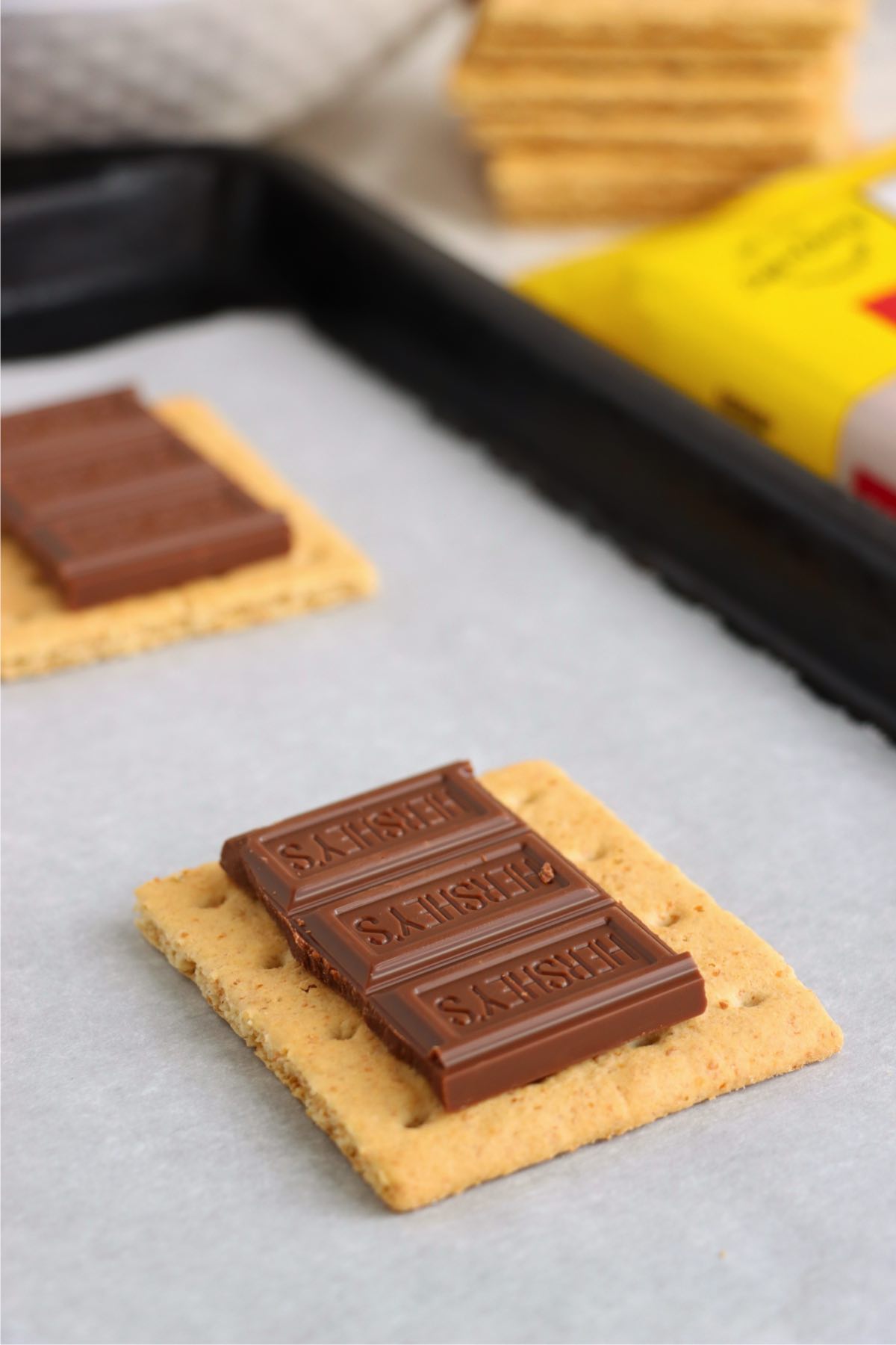 Three squares of Hershey's milk chocolate resting on a graham cracker square on a parchment-lined baking sheet.