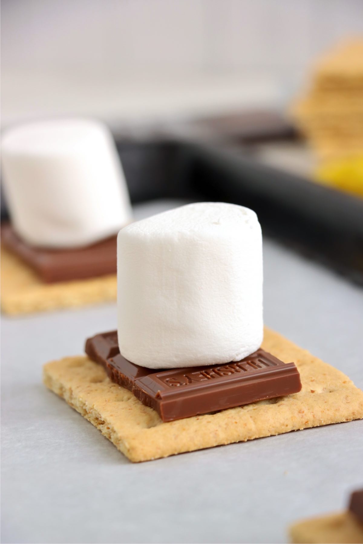 Large white marshmallow sitting upright on milk chocolate pieces and a square graham cracker.