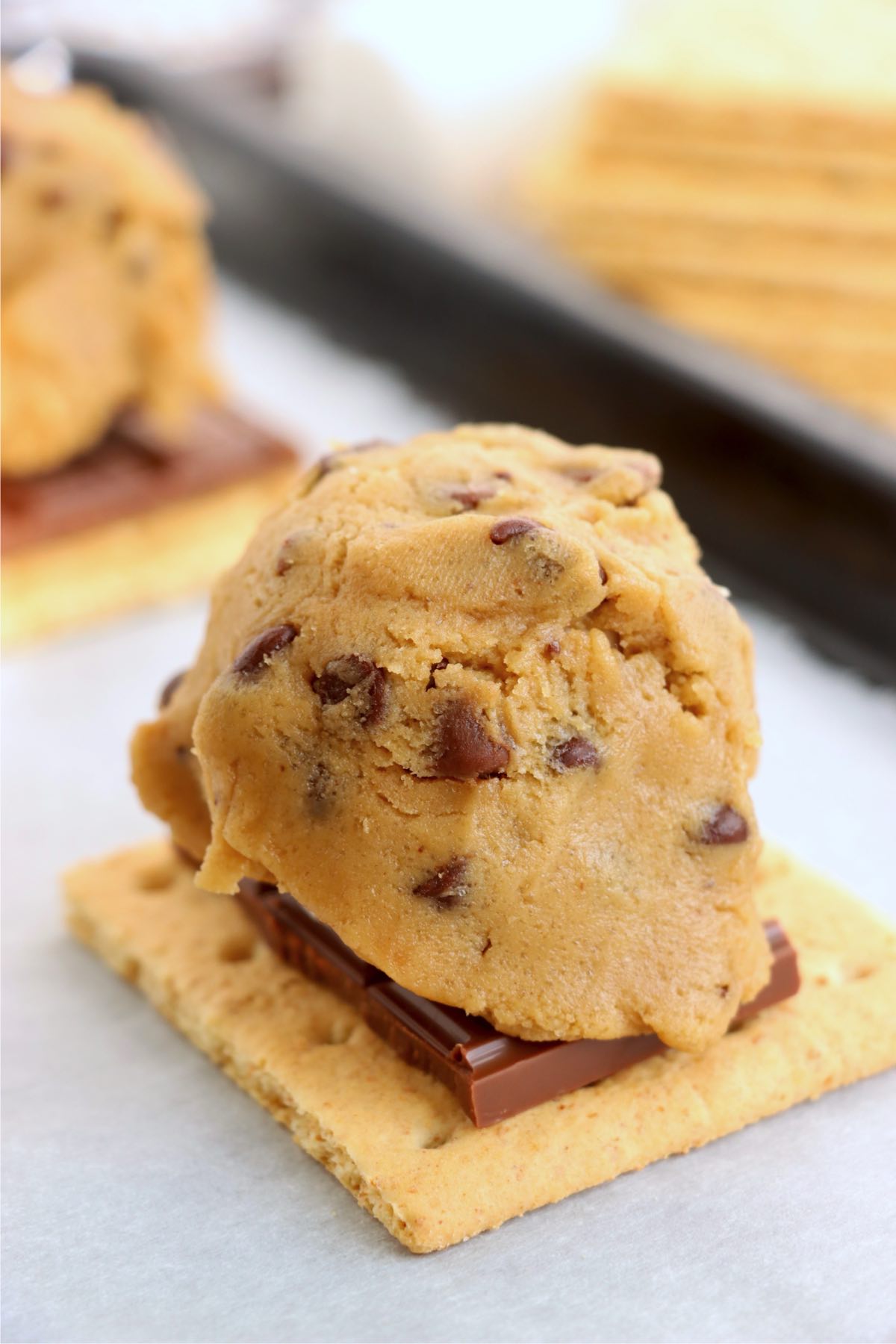 Scoop of chocolate chip cookie dough covering a marshmallow and chocolate on a graham cracker.