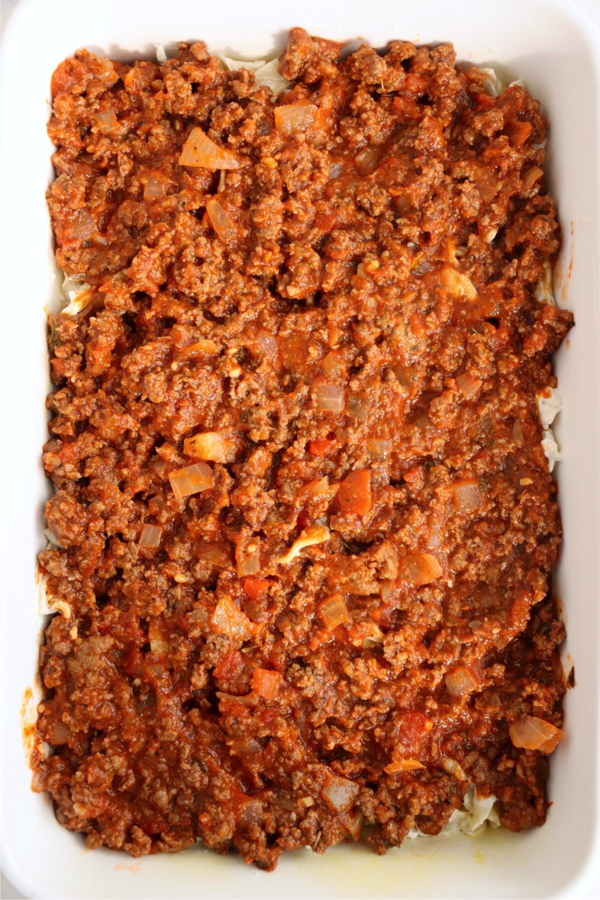 Rich ground beef and tomato sauce spread over creamy egg noodles in a white rectangular baking dish.