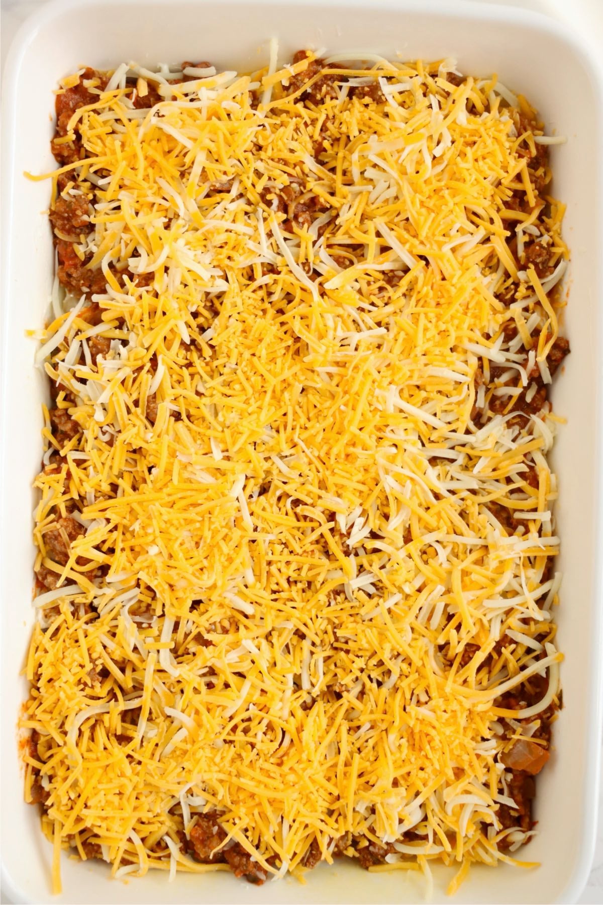 Ground beef casserole topped generously with shredded Colby Jack and cheddar cheeses before baking.