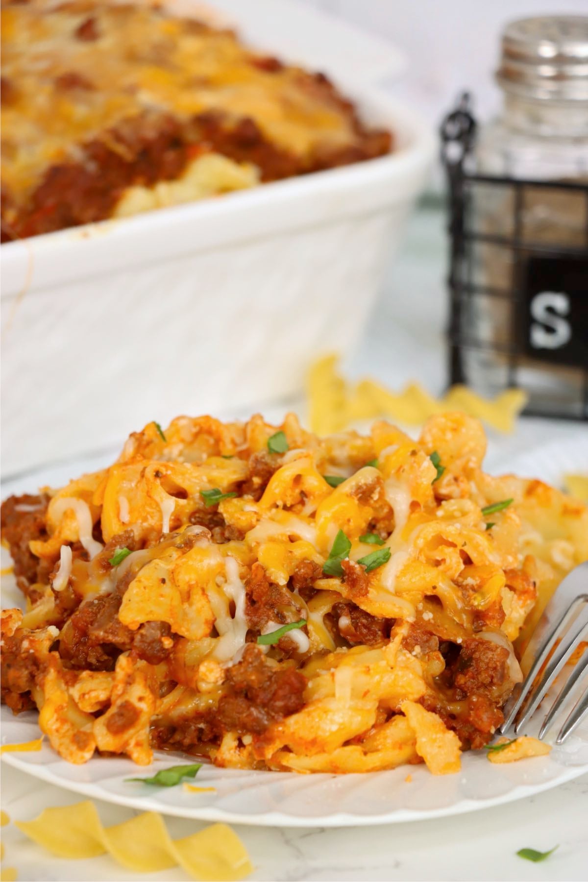 Cheesy beef and egg noodle casserole served on a white plate with fresh chopped parsley.