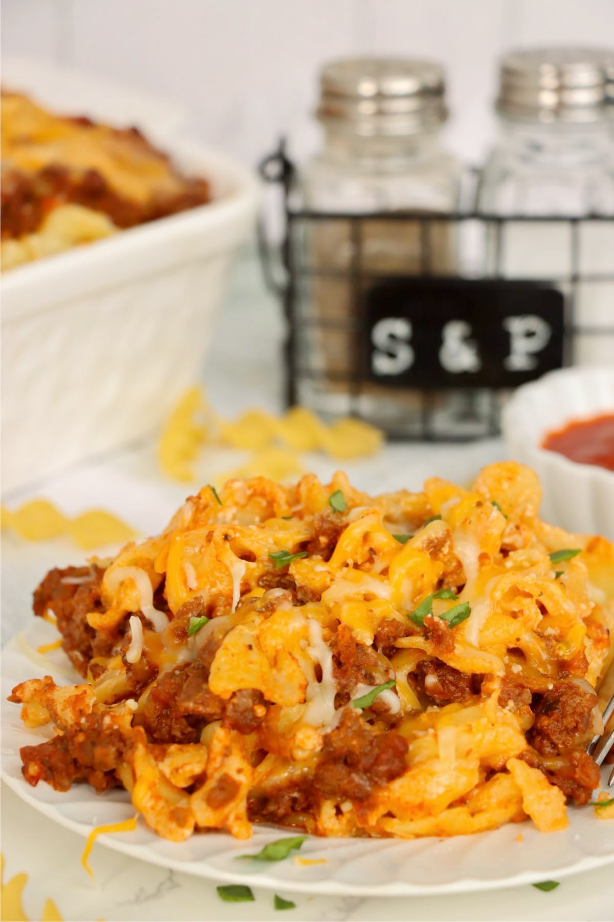 Warm cheesy beef and noodle casserole plated beside baking dish and salt and pepper shakers.