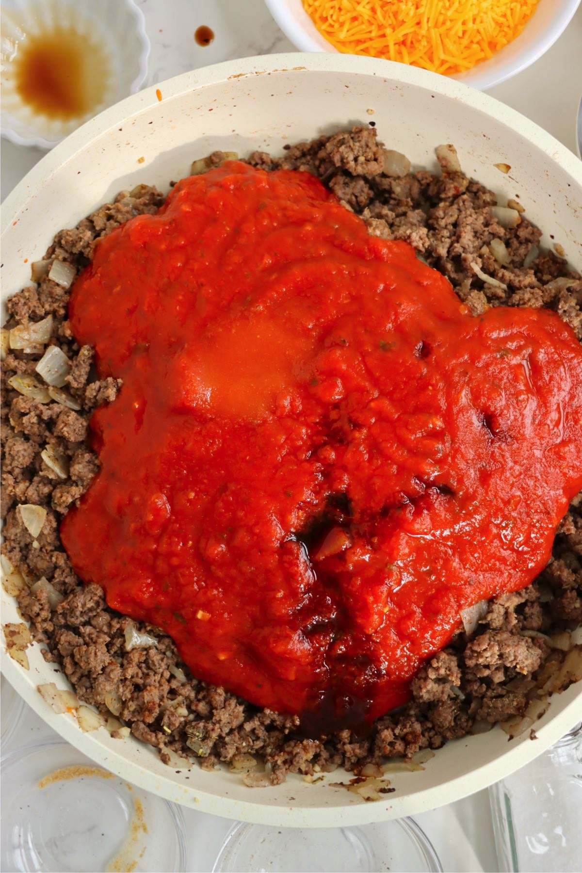 Red tomato sauce and Worcestershire sauce added over seasoned browned ground beef and onions in skillet.