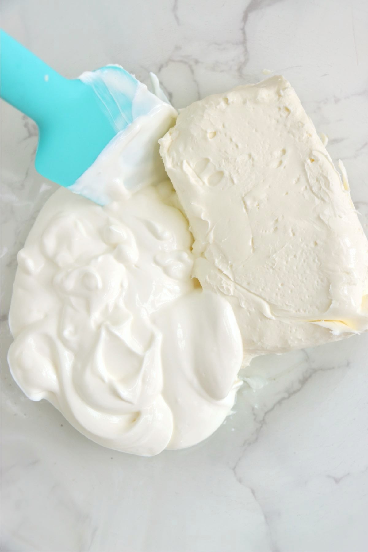 Softened cream cheese and sour cream placed together in a mixing bowl with a silicone spatula.